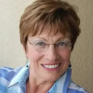 A woman with glasses and short hair wearing a blue shirt.